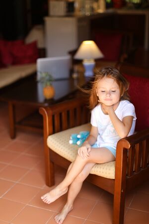 Little european female kid sitting with toy in wooden chair. Concept of kid model and wood in interior.の写真素材