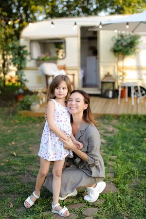 Young mother hugging little female kid near house on wheels. Concept of summer vacations and family.の写真素材