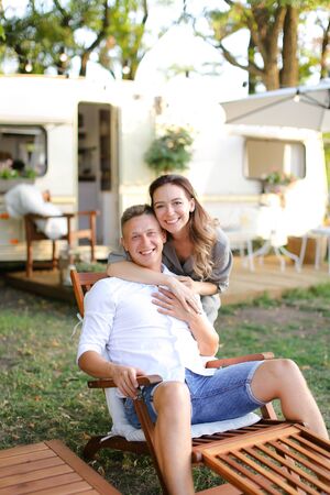 Young happy man and woman sitting in wooden chair near house on wheels. Concept of happy couple and summer vacations.の写真素材