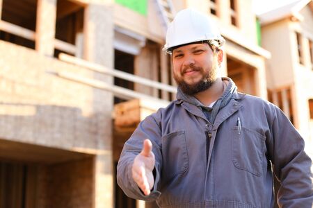 Caucaisan foreman wearing hardhat and giving hand for shaking on construction site, brick building in background. Concept of real estate and professions.の写真素材