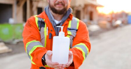 Banner of focus on disinfectant soap given by engineer wearing orange workwear and hardhat at construction site. Concept of corona virus protection and disinfectant for washing hands.の写真素材