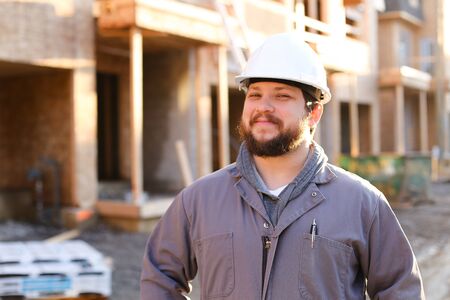 Portrait of american engineer or builder wearing hardhat on construction site, brick building in background. Concept of professions and working abroad, real estate.の写真素材