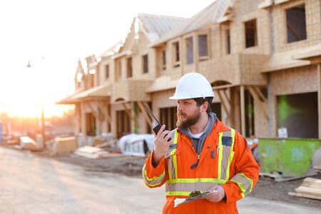 Foreman talking by walkie talkie on construction site and holding notebook. Concept of building house and architectural profession.の写真素材