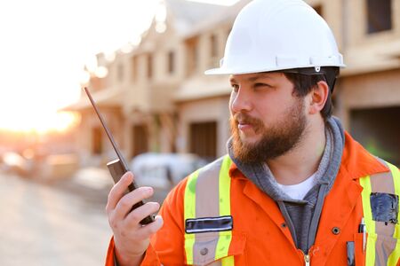 Portrait of caucasian foreman talking by walkie talkie on construction site. Concept of building house and architectural profession.の写真素材