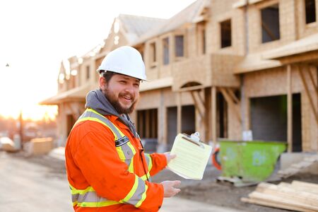 European foreman in orange workwear holding notebook on construction site, house in background. Concept of real estate in Europe.の写真素材