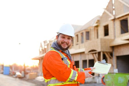 American foreman in orange workwear holding notebook on construction site, house in background. Concept of real estate in USA.の写真素材