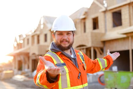 Portrait of architect or builder in white helmet showing keys fand new house on construction site. Concept of properties for sale and real estate.の写真素材