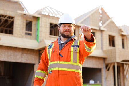 Portrait of smiling engineer giving keys from new house on construction site. Concept of properties for sale and real estate.の写真素材