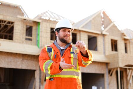 Portrait of euroepan engineer giving keys from new house on construction site. Concept of properties...