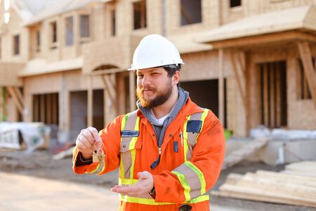 Portrait of foreman or builder in white helmet giving keys from new house on construction site. Concept of properties for sale and real estate.の写真素材