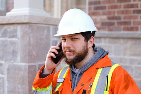 Portrait of foreman or builder in hardhat talkign by smartphone outdoors. Concept of modern...