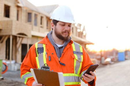 Architect surfing internet by smartphone and holding notebook on construction site. Concept of building house and real estate in USA.の写真素材