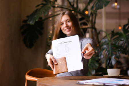 Focus on visa aplication and passport in young european woman hands at travel agency cabinet. Concept of execution of document for emigration.の写真素材