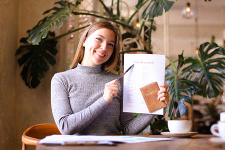 Young caucasian woman filling visa application and holding passport at cabinet. Concept of travel agency and execution of documents.の写真素材