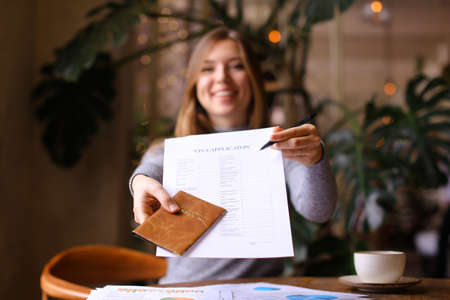 Focus on visa aplication and passport in young woman hands at travel agency cabinet. Concept of execution of document for emigration.の写真素材