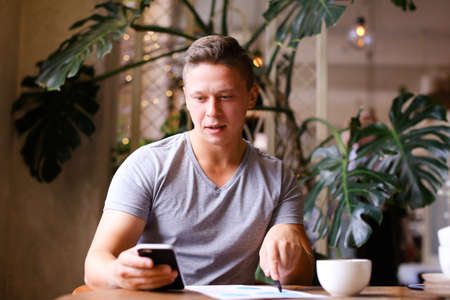 Young confident caucasian businessman working with documents and smartphone at cafe. Concept of break and freelance.の写真素材