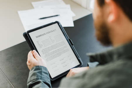 Close up man reading electronic template of marriage contract on tablet at office. Concept of filling documents and wedding papers.の写真素材