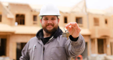 Banner, focus on apartment keys, foreman giving and wearing hardhat at construction site. Concept of purchasing flat and house building.の写真素材