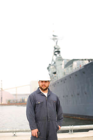 Deck Officer wearing helmet and holding VHF walkie talkie radio in hands, standing on the coast with...