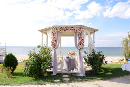 Nice wedding arch decorated by roses with lake in background. Concept of outdoor bridal ceremony place.の写真素材