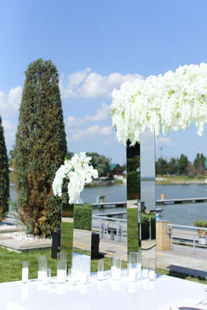 White wonderful wedding arch decorated by flowers with lake in backround. Concept of bridal outdoor ceremony place.の写真素材