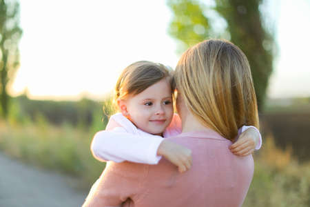 Blonde caucasian young woman holding female kid and walking on road. Concept of family photo session...