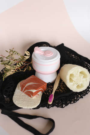 Wooden toothbrush, white bottle with handmade eco soap, natural loofah sponge on mesh bag background...