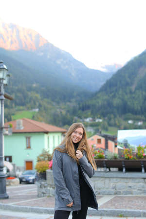 Young woman standing in little village with mountains and building in background. Concept of rustic resort and european town.の写真素材