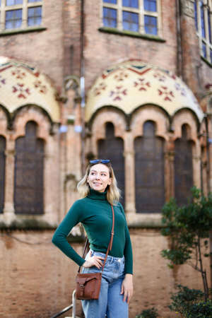 Young blonde nice woman standing near old building in Europe and wearing green turtleneck sweater. Concept of european architecture and traveling.の写真素材