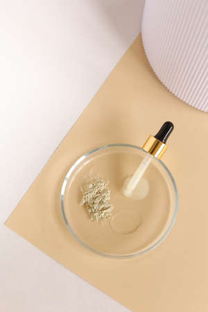Clay powder and water in glass jar near pipette on beige and white background. Concept of making facial mask ingredients, homemade cosmetics and organic cosmetic.の写真素材
