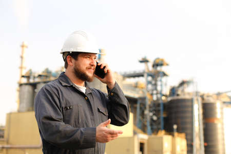 Portrait of industrial director speaking by VHF walkie talkie near factory outside. Man wearing...