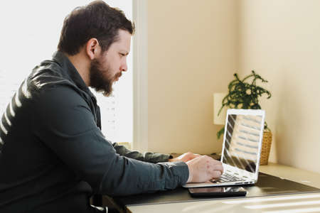 Young bearded businessman working in office, looking at laptop computer screen. Concep of web design and modern technology, private business investor.の写真素材
