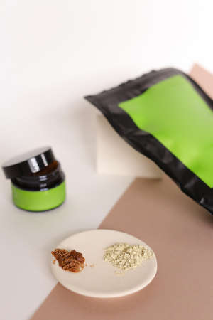 Focus on white plate with clay powder near doypack and jar with cosmetic products and green space for your brand. Concept of facial mask ingredients and homemade organic cluelty free, kosher cosmetic for skin and pampering.の写真素材