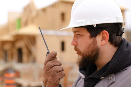 Portrait of builder talking by walkie talkie at construction site, wearing hardhat. Concept of architectural profession and house building.の写真素材