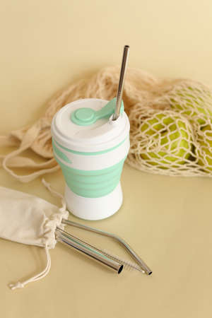 Silicone straw cup with stainless steel straws on beige background with mesh bag with fruits....