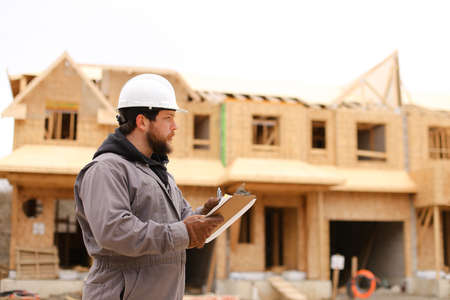 Male builder drawing plan in notebook at construction site and wearing hardhat. Concept of architectural profession and house building.の写真素材
