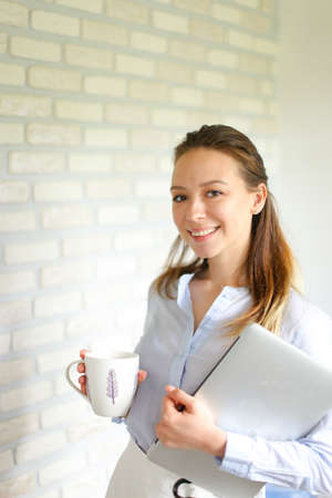 Portrait of young caucasian businesswoman standing with documents and cup of coffee. Concept of secretary job, business person and office occupation.の写真素材