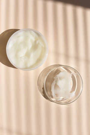 Natural ecofriendly handmade facial cream in white jar, striped shadow background.