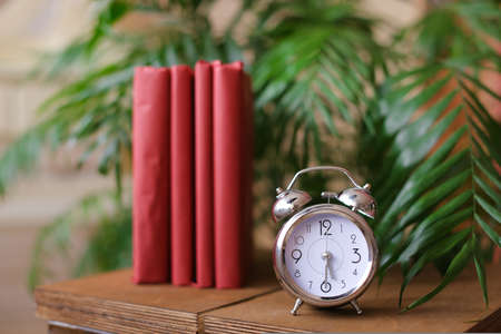 Red stylish photo albums stnding near clock and houseplant on table.の写真素材