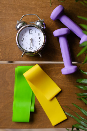 Alarm clock and women dumbbells lying on wooden table.の写真素材