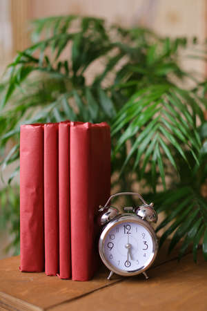 Red photo albums stnding near clock and houseplant on table.の写真素材