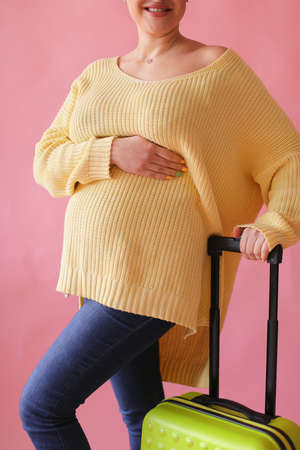 Pregant woman standing with valise in pink background.の写真素材