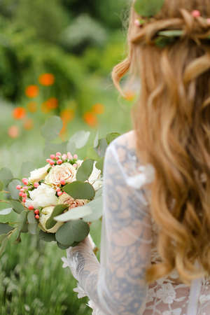 Back view portrait of young bride with bouquet walking in field.の写真素材