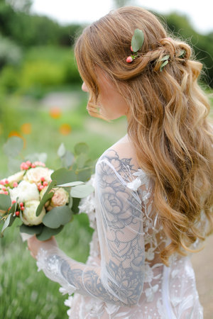 Back view portrait of bride with bouquet walking in field.の写真素材