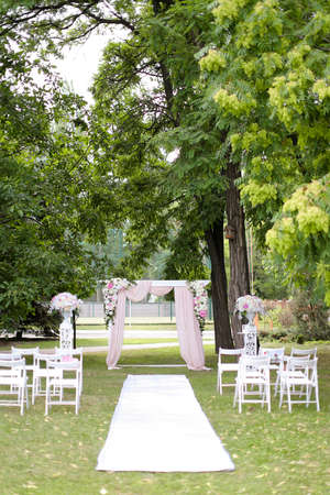 Wedding expensive arch, decorated by roses and chairs in park.の写真素材