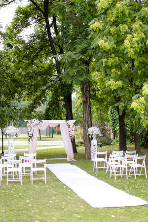 Wedding amazing arch, decorated by roses and chairs in park.の写真素材