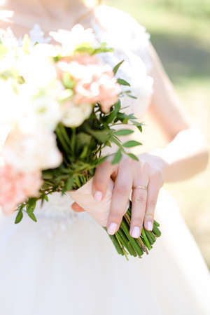 Focus on golden wedding ring, bride keeping bouquet of roses.の写真素材