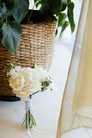Bridal bouquet of white flowers near basket with houseplants. Concept of wedding morning photo session.の写真素材