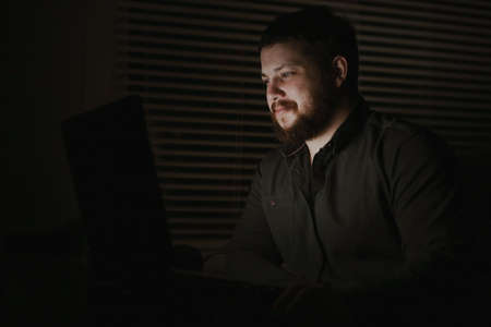 Young male computer hacker working with laptop lately at night.の写真素材