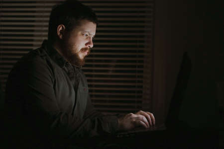 Young male freelancer working with laptop lately at night.の写真素材